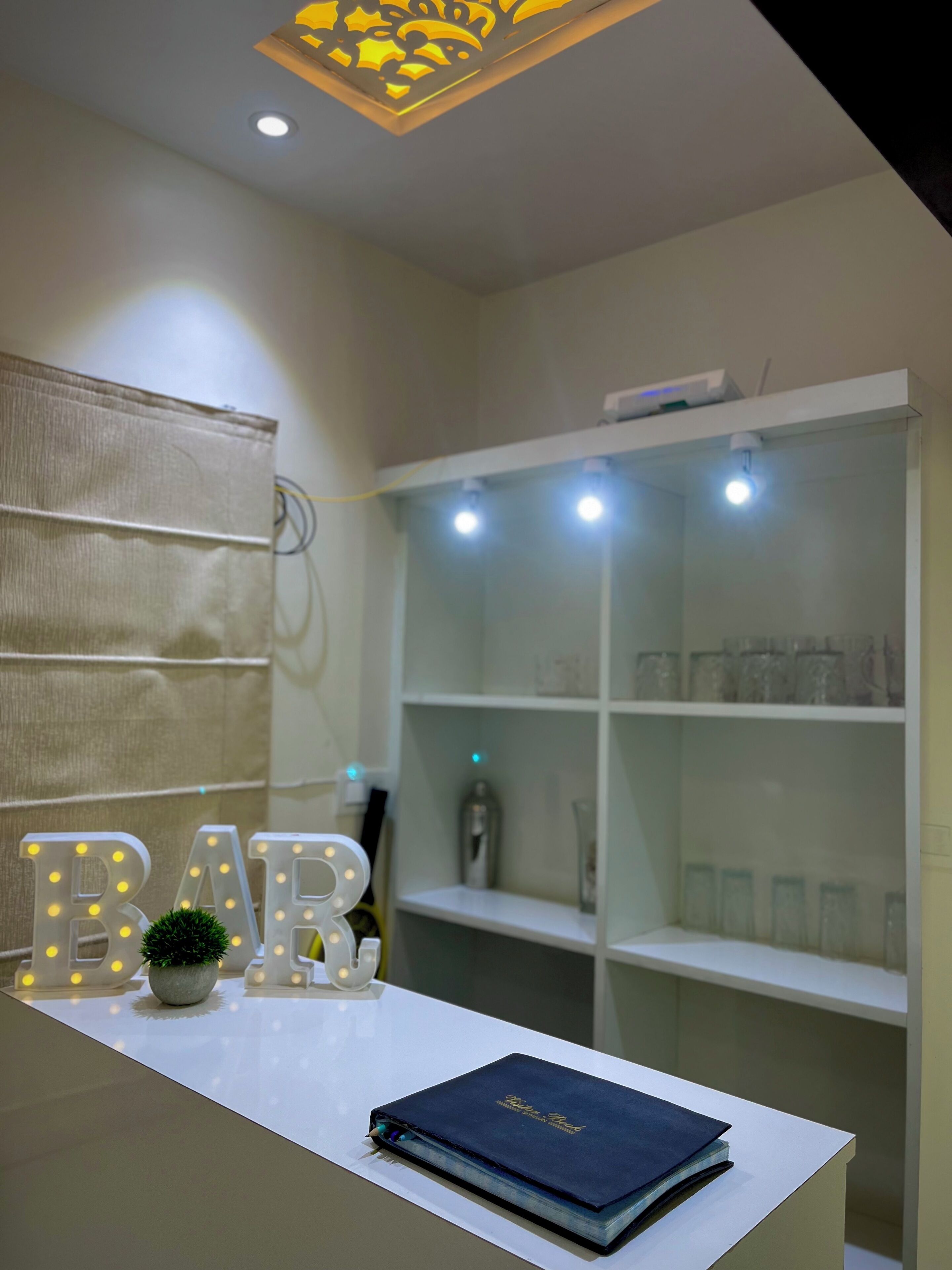 Une pièce avec un bureau blanc, un luminaire décoratif et une étagère contenant de la verrerie.