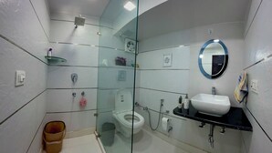 A modern bathroom with a glass-enclosed shower, a white toilet, a sink with a mirror, and a small trash bin. - Patio Paradise, Pitampura
Cozy and peaceful 3BHK Condo (New delhi)