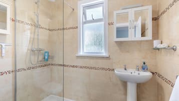 A bathroom with a glass-enclosed shower, a bathtub, a sink, and a window.
