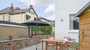 A patio with a table and chairs, a hanging umbrella, and potted plants. - 1 bedroom accommodation in Torquay (Torquay)