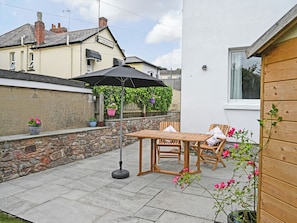 A patio with a table and chairs, a hanging umbrella, and potted plants.