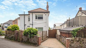 A two-story residential house with a tiled roof, a brick chimney, and a paved driveway leading to a gated entrance. - 1 bedroom accommodation in Torquay (Torquay)