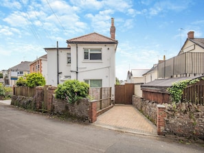 A two-story residential house with a tiled roof, a brick chimney, and a paved driveway leading to a gated entrance.