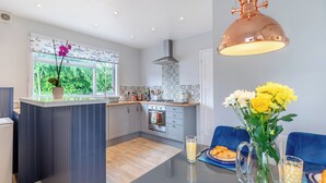 A modern kitchen with a central island, a dining area with a table and chairs, and a view of the outdoors through a window. - 1 bedroom accommodation in Torquay (Torquay)