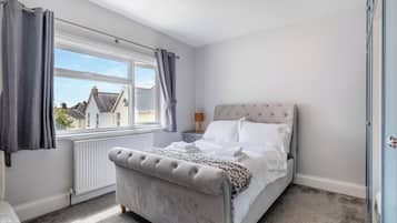 A bedroom with a bed, a window, a radiator, and a light fixture.