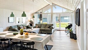 Ein geräumiges Zimmer mit hoher Decke, Holzvertäfelung, einem Essbereich mit Tisch für vier Personen und einer großen Glasschiebetür, die zu einem Außenbereich führt.
