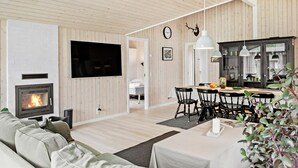 Ein modernes Wohnzimmer mit Kamin, Wand-Fernseher und Essbereich mit Tisch und Stühlen.