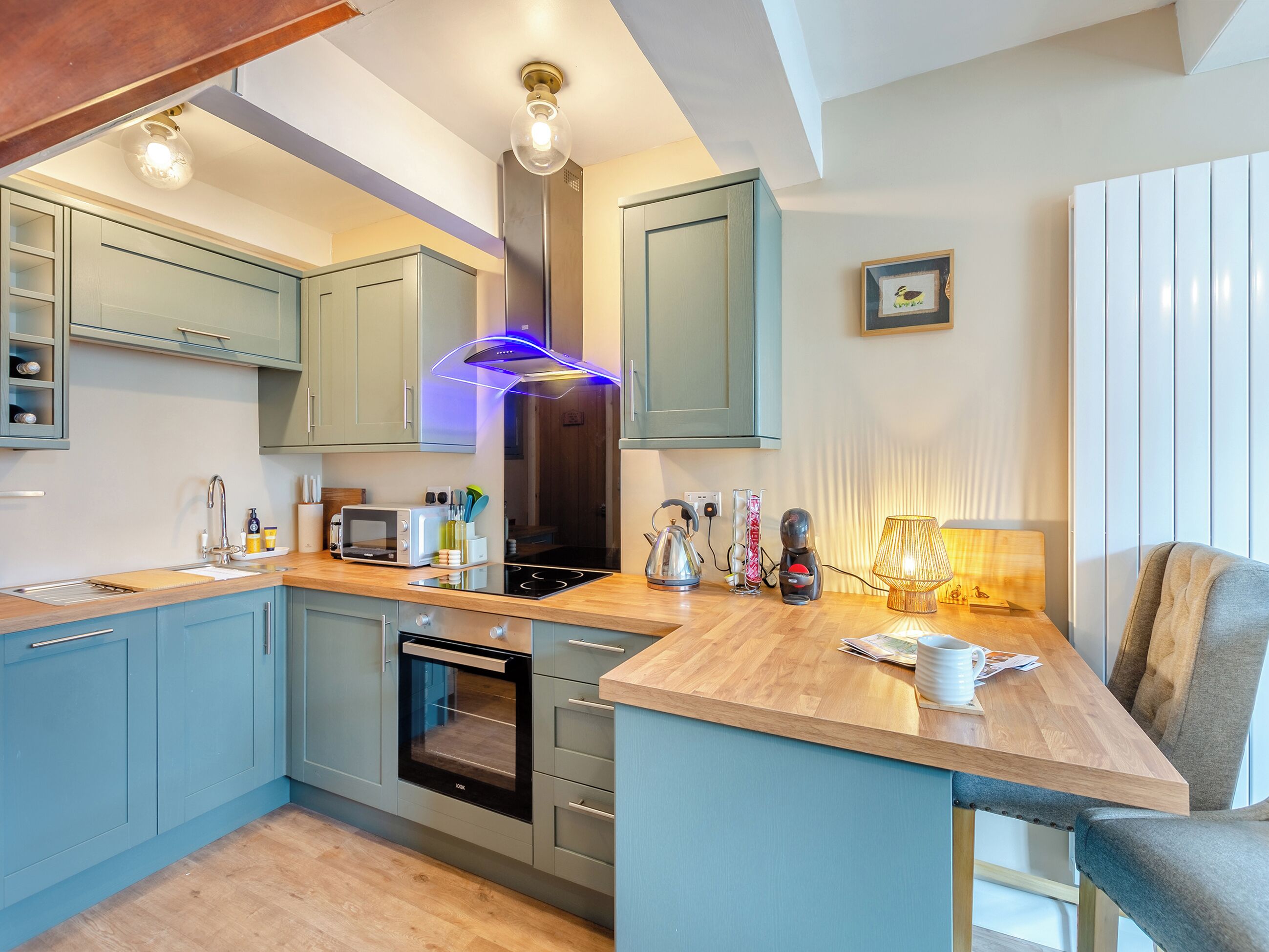 A modern kitchen with light blue cabinets, a built-in oven, a microwave, and a kettle on the counter.