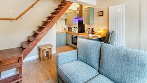 Una cocina moderna con una escalera de madera, un área de comedor con un sofá azul y una mesita.