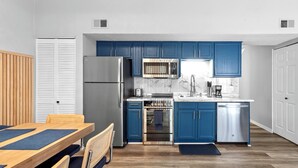 A compact kitchen with blue cabinets, stainless steel appliances, and a dining area with a wooden table and chairs. - Stunning Condo Near Lake 2BR 2BA  right in Branson! Sleeps 6 .  (Branson)