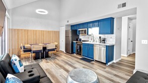 A modern kitchen with blue cabinets, a dining area with a wooden panel wall, and a black leather sofa with a round ottoman. - Stunning Condo Near Lake 2BR 2BA  right in Branson! Sleeps 6 .  (Branson)