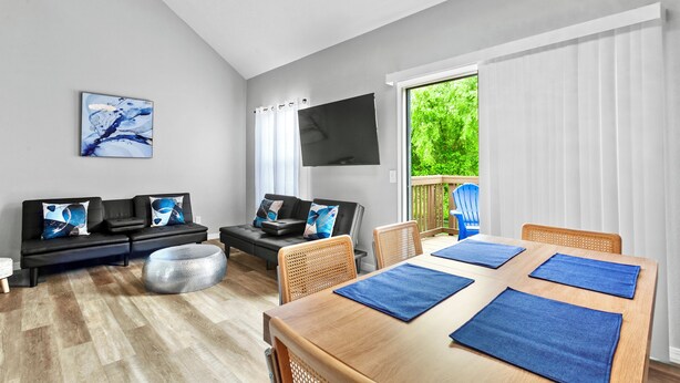 A modern living room with a sofa, ottoman, and a dining table with blue placemats. - Stunning Condo Near Lake 2BR 2BA  right in Branson! Sleeps 6 .  (Branson)