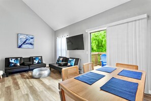 A modern living room with a sofa, ottoman, and a dining table with blue placemats.