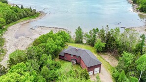 A house with a red roof and white garage doors, surrounded by dense green trees and a large body of water. - Designer Oceanfront, Views of Acadia National Park, Near Bar Harbor (Trenton)