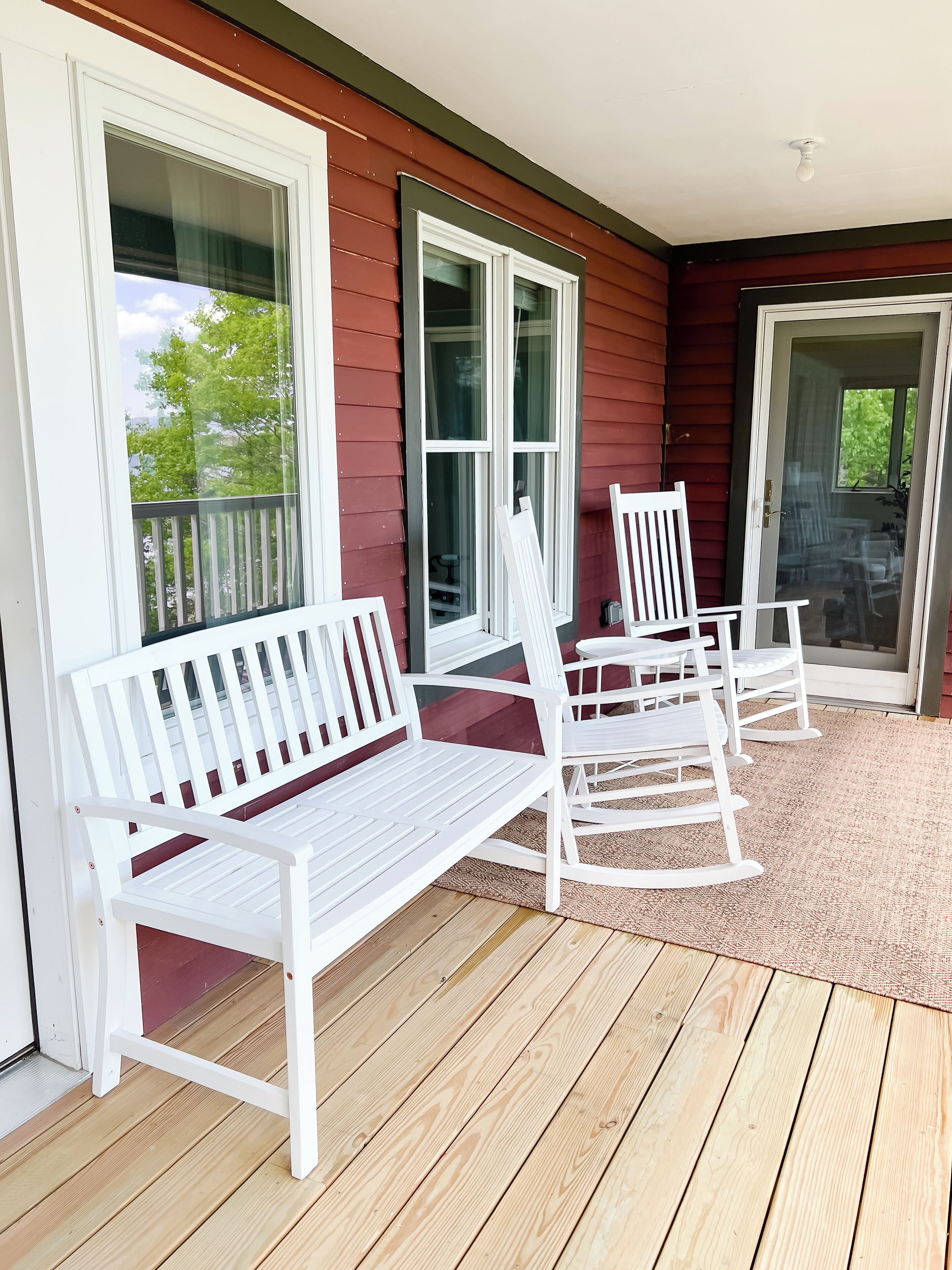 A covered porch with a wooden deck, white rocking chairs, and a bench.