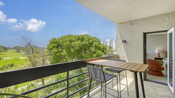 Enjoy a serene view of the golf course from this room's balcony, featuring a table and two chairs.