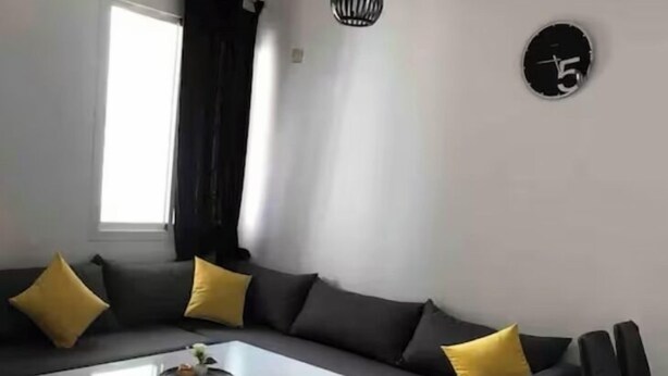 Ein modernes Wohnzimmer mit einem grauen Sofa, gelben Kissen, einem weißen Couchtisch und einem schwarzen Teppich.