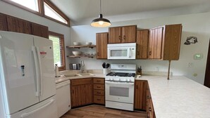 Una cucina con mobili in legno, un frigorifero bianco, un forno a microonde, un piano cottura e un lampadario.