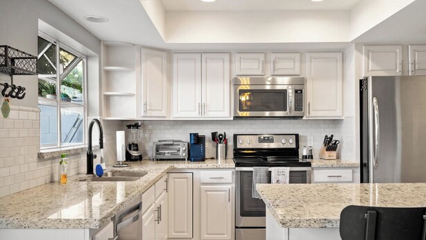 A modern kitchen with white cabinets, stainless steel appliances, a granite countertop, and a window providing natural light. - Ideal Old Town Scottsdale Location! Perfect for Families. Camelback Mt. View! (Scottsdale)