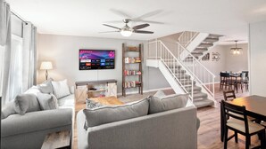 A modern living room with a grey sofa set, a flat-screen TV, a bookshelf, and a staircase leading to a dining area. - Ideal Old Town Scottsdale Location! Perfect for Families. Camelback Mt. View! (Scottsdale)