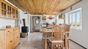 A kitchen with wooden cabinets, a stove, and a dining area with chairs and a table. - Nice home in Harboøre with WiFi (Harboøre)
