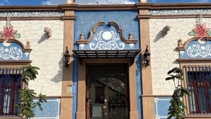 Une façade d’immeuble ornée d’éléments décoratifs bleus et beiges, avec une entrée centrale et deux petits arbres devant.