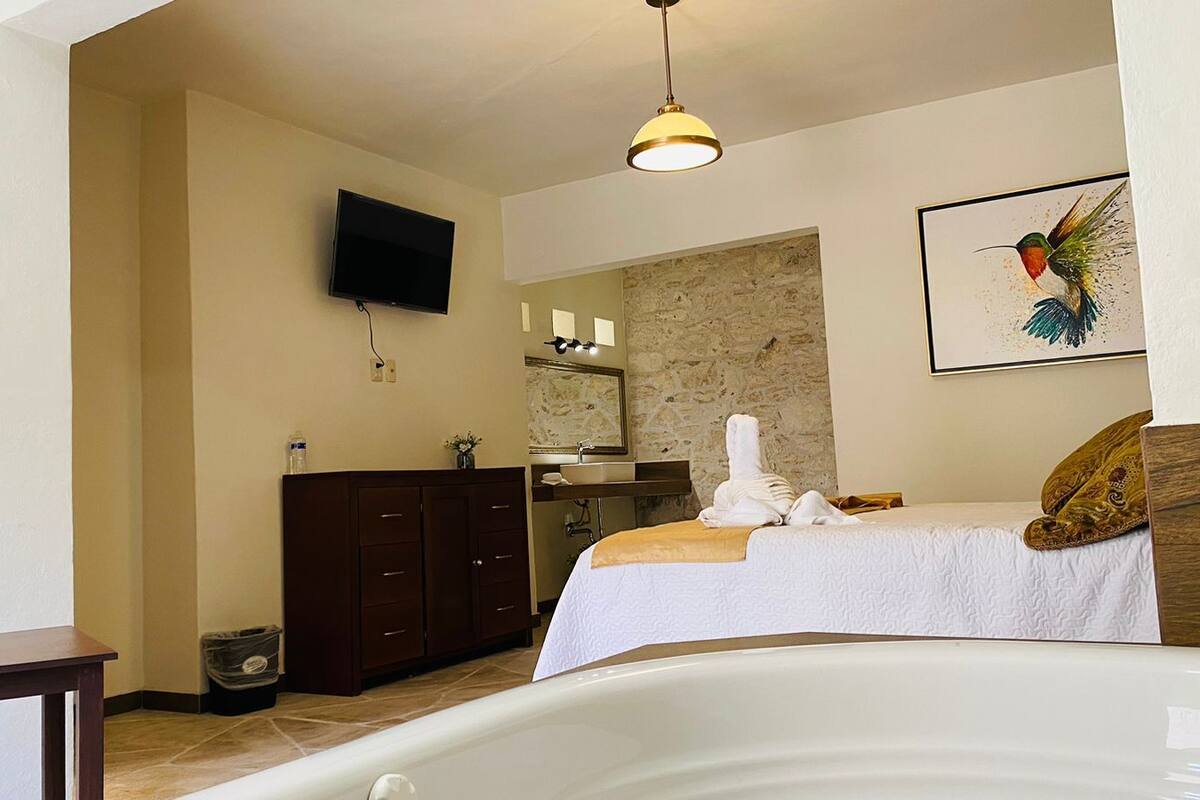 Un dormitorio con una cama, un aparador de madera, un televisor, una pared de piedra y un cuadro de un colibrí.