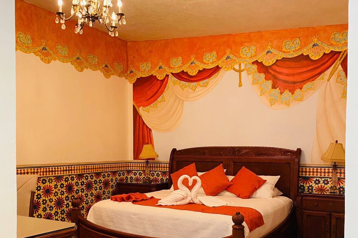 Un dormitorio con una cama de madera, cortinas ornamentadas, una araña y un papel tapiz estampado.