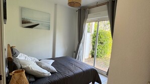 A bedroom with a bed, a bedside table, a lamp, a painting on the wall, and a view of greenery outside.