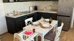 Et kompakt køkken med mørke skabe, et rustfrit stål køleskab og et spisebord med plads til to personer.