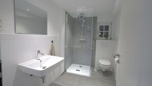 Une salle de bain moderne avec une douche à parois de verre, un lavabo blanc et des toilettes.
