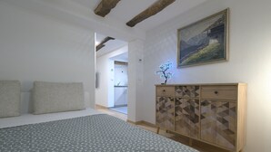Une chambre à coucher avec un lit, une commode, un tableau et un couloir menant à une autre pièce.