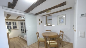 Un coin repas avec une table et des chaises en bois, un ventilateur de plafond et une fenêtre donnant sur un lit.