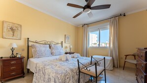 A hotel room with a bed, a desk, a chair, a dresser, a ceiling fan, and a window with curtains. - MalagaSuite Costa Sol Oasis 3 (Torremolinos)