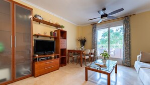 A living room with a TV, wooden furniture, a ceiling fan, and a balcony with a view. - MalagaSuite Costa Sol Oasis 3 (Torremolinos)