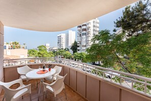 Een balkon met een tafel en stoelen, met uitzicht op een stadsgezicht met hoge gebouwen en bomen.