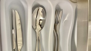 Bandeja blanca con tres compartimentos que contienen un cuchillo, una cuchara y un tenedor.