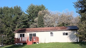 A single-story house with a red front porch and a small deck, surrounded by a grassy yard and trees. - Peaceful Vacation Home Near Wisconsin Delles with the pond on 80 Wooded Acres. (Lyndon Station)