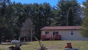 A house with a red roof and a small porch. There is a grassy yard with a tree and a metal tank in the background. - Peaceful Vacation Home Near Wisconsin Delles with the pond on 80 Wooded Acres. (Lyndon Station)