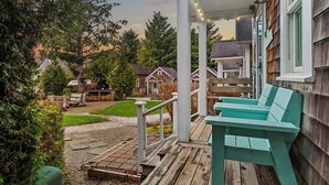 A wooden deck with a green bench, a covered porch with string lights, and a view of a residential area with houses and trees. - Seabrook Cabin - Private HotTub & Backyard, 10 minute Walk to Town, Dog Friendly (Pacific Beach)
