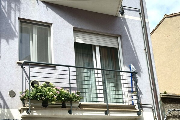 Un immeuble doté d’un balcon, d’une fenêtre avec un store enrouleur et d’un pot de fleurs.