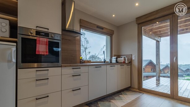 A modern kitchen with stainless steel appliances, a large window, and a view of wooden cabins. - L'alticime - LA Feclaz LES Deserts (LA FECLAZ LES DESERTS)