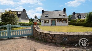 Une maison traditionnelle en pierre, avec une porte verte, entourée d’un mur de pierre et d’un portail bleu.