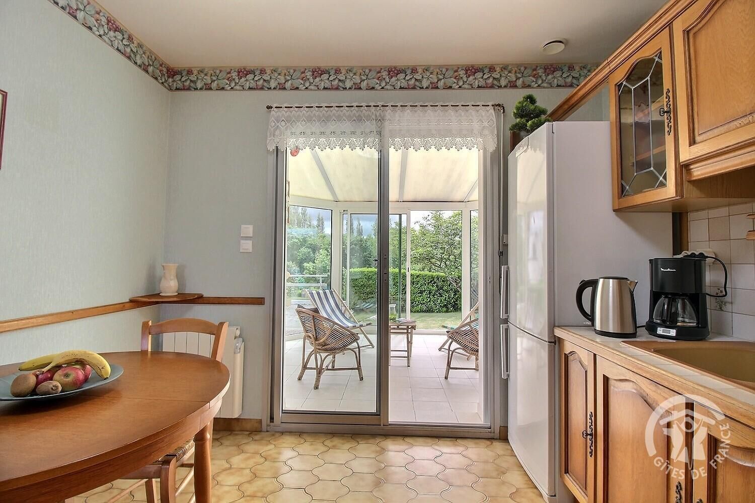A compact kitchen with a dining area, a refrigerator, a coffee maker, and a view of a garden through a sliding glass door.