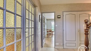 Un couloir avec un mur orné de motifs, une porte en bois et un escalier doté d’une balustrade.