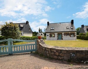 Een klassiek stenen huis met een groene deur, omgeven door een stenen muur en een blauw hek.
