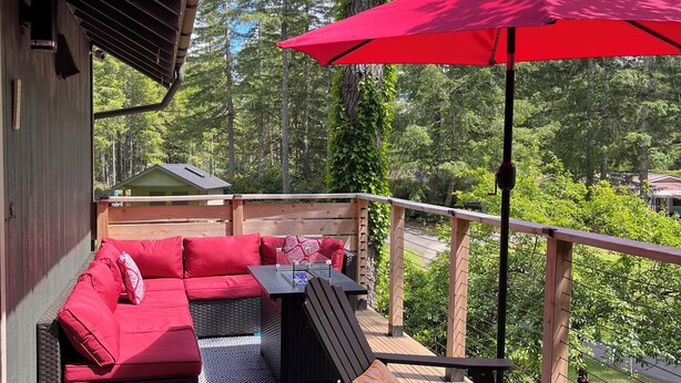 An outdoor deck with a red umbrella, wicker furniture, and a view of the forest. - Modern Alderbrook pet-friendly retreat.   (Union)