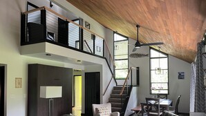 A modern living room with a large sectional sofa, a dining area with a table and chairs, a staircase with a wooden railing, and large windows allowing natural light. - Modern Alderbrook pet-friendly retreat.   (Union)