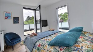A bedroom with a bed, a chair, a TV, and a balcony with a view.