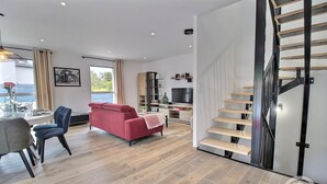 A modern living room with a red sofa, a dining table with chairs, a staircase with wooden steps, and a television.